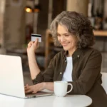 Consumidora 50+ fazendo compra pela internet com notebook e cartão