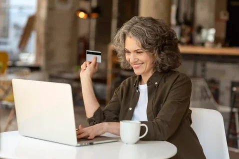 Consumidora 50+ fazendo compra pela internet com notebook e cartão