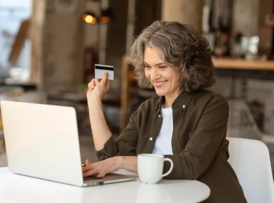 Consumidora 50+ fazendo compra pela internet com notebook e cartão