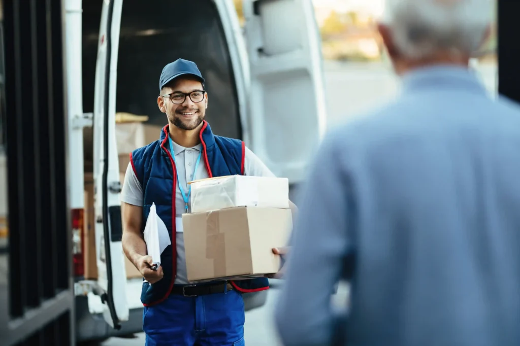 Entregador segura duas caixas diante de uma van de entregas enquanto conversa com um cliente
