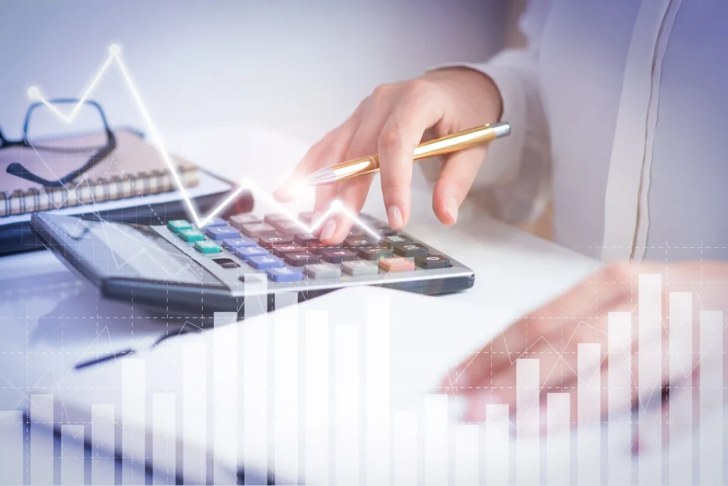 Pessoa usa calculadora sobre uma mesa enquanto gráficos de linhas e barras aparecem sobrepostos à imagem