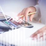 Pessoa usa calculadora sobre uma mesa enquanto gráficos de linhas e barras aparecem sobrepostos à imagem