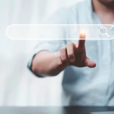 Pessoa tocando uma barra de pesquisa digital com ícone de lupa, representando a busca com IA e a descoberta de produtos nas recomendações online