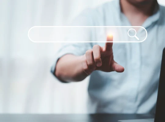 Pessoa tocando uma barra de pesquisa digital com ícone de lupa, representando a busca com IA e a descoberta de produtos nas recomendações online