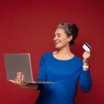 Mulher madura usando notebook e segurando cartão para fazer uma compra online