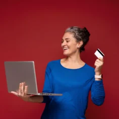 Mulher madura usando notebook e segurando cartão para fazer uma compra online