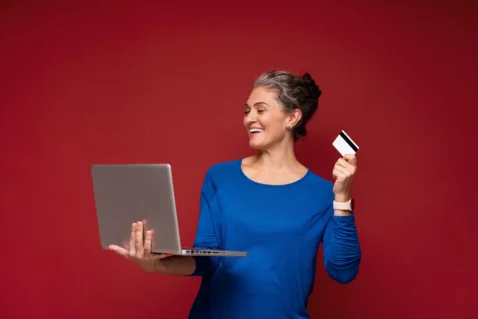 Mulher madura usando notebook e segurando cartão para fazer uma compra online