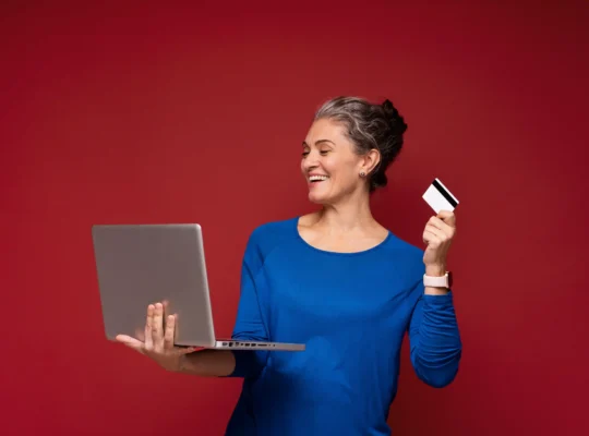 Mulher madura usando notebook e segurando cartão para fazer uma compra online