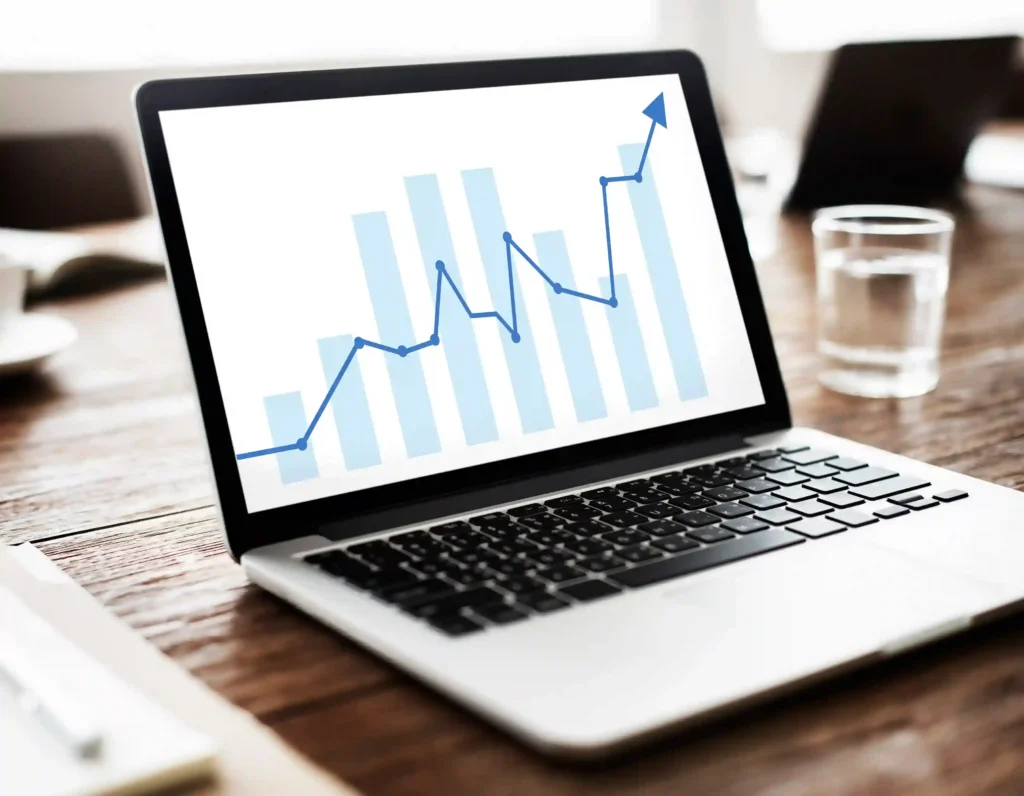 Notebook sobre uma mesa exibindo gráfico de barras e linha em crescimento na tela, representando o aumento das vendas online