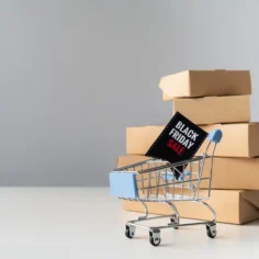 Carrinho de compras com placa de Black Friday diante de caixas de produtos representando a preparação do estoque Black Friday 2026