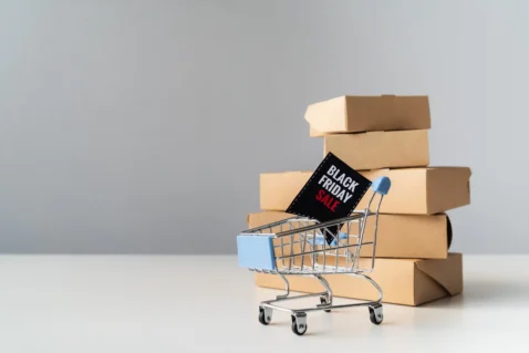 Carrinho de compras com placa de Black Friday diante de caixas de produtos representando a preparação do estoque Black Friday 2026