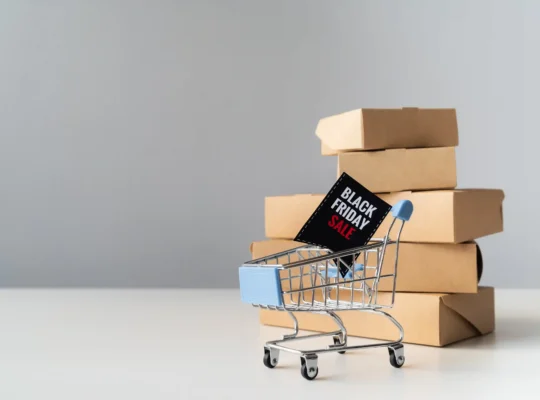 Carrinho de compras com placa de Black Friday diante de caixas de produtos representando a preparação do estoque Black Friday 2026