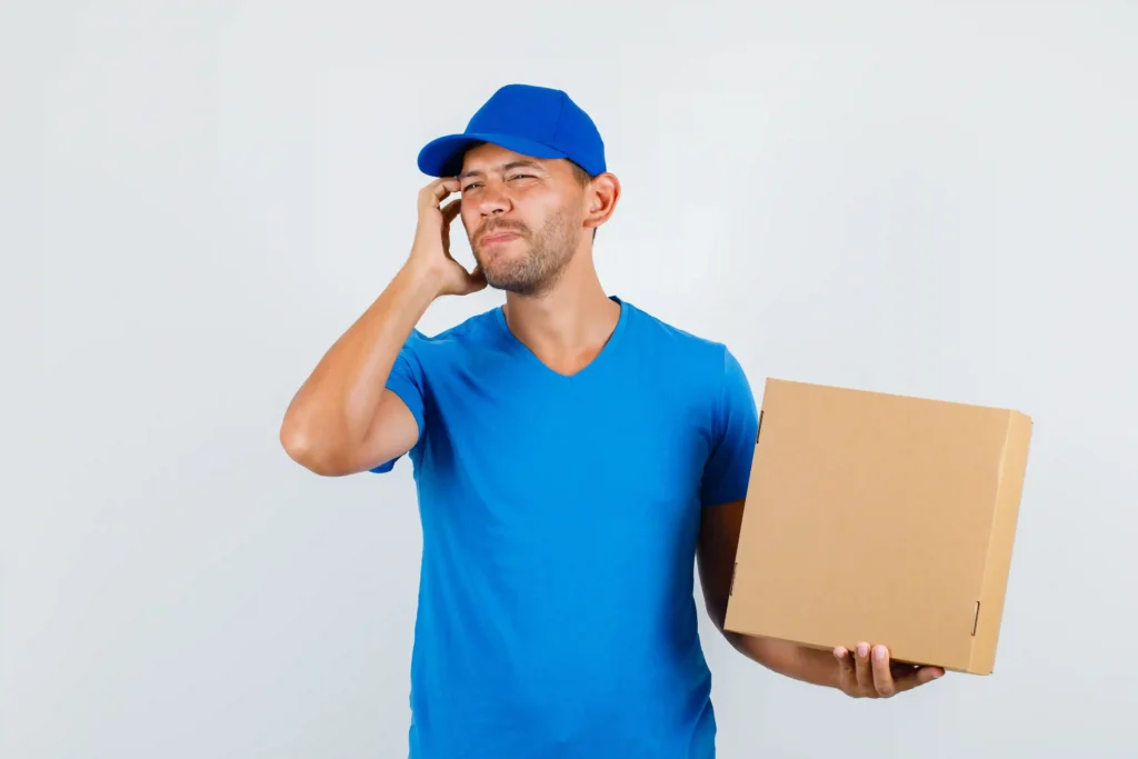 Entregador segurando uma caixa e falando ao telefone, em uma cena que representa a comunicação com o consumidor diante de atraso na entrega