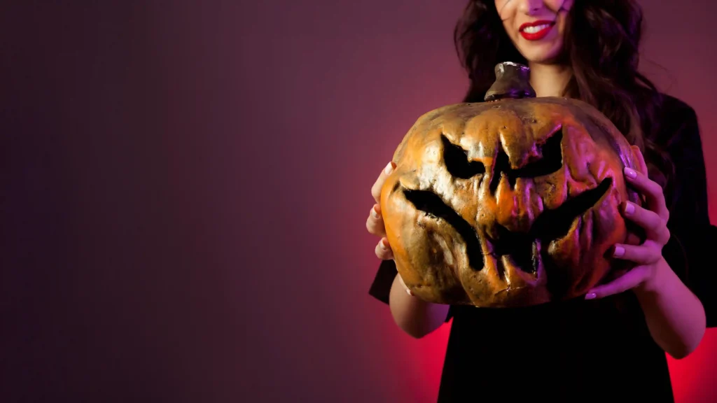 Mulher segurando uma abóbora decorada para o Halloween em fundo vinho