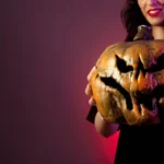 Mulher segurando uma abóbora decorada para o Halloween em fundo vinho
