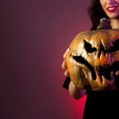 Mulher segurando uma abóbora decorada para o Halloween em fundo vinho