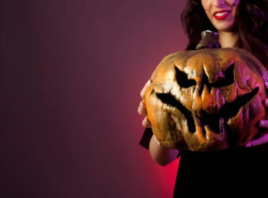 Mulher segurando uma abóbora decorada para o Halloween em fundo vinho