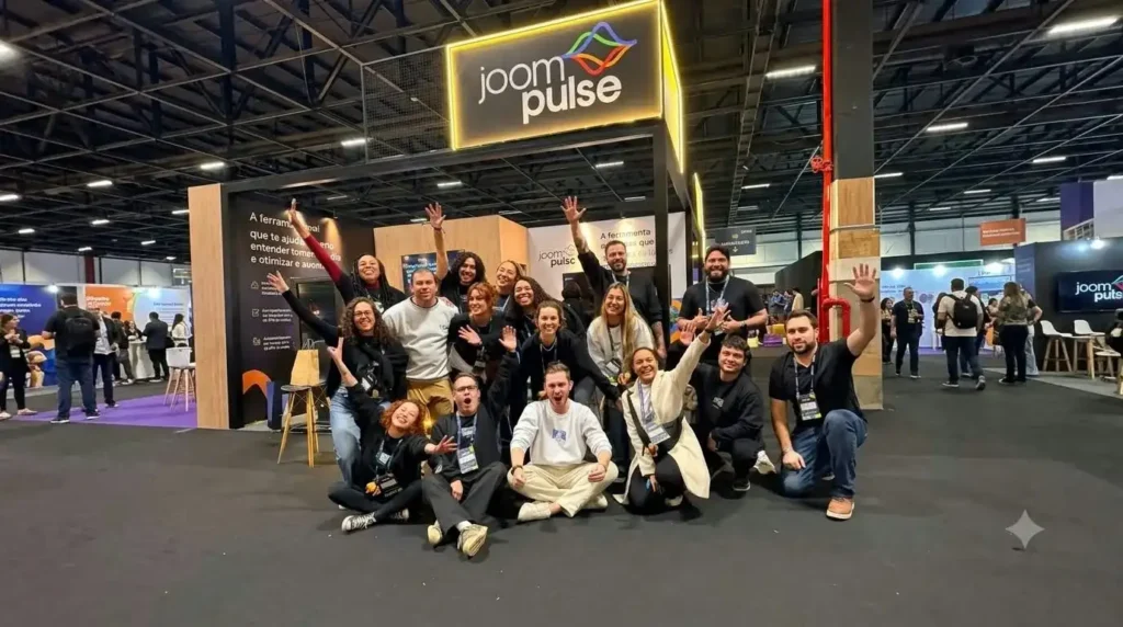 Equipe da JoomPulse reunida em frente ao estande da empresa durante um evento de e-commerce, com o logotipo da JoomPulse iluminado acima do grupo