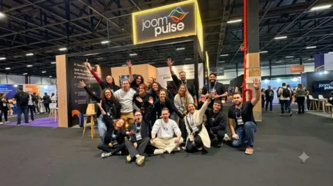 Equipe da JoomPulse reunida em frente ao estande da empresa durante um evento de e-commerce, com o logotipo da JoomPulse iluminado acima do grupo