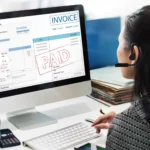 Mulher usando headset diante de computador com notas fiscais e comprovantes de pagamento na tela, representando a emissão de nota fiscal ecommerce para vendas online