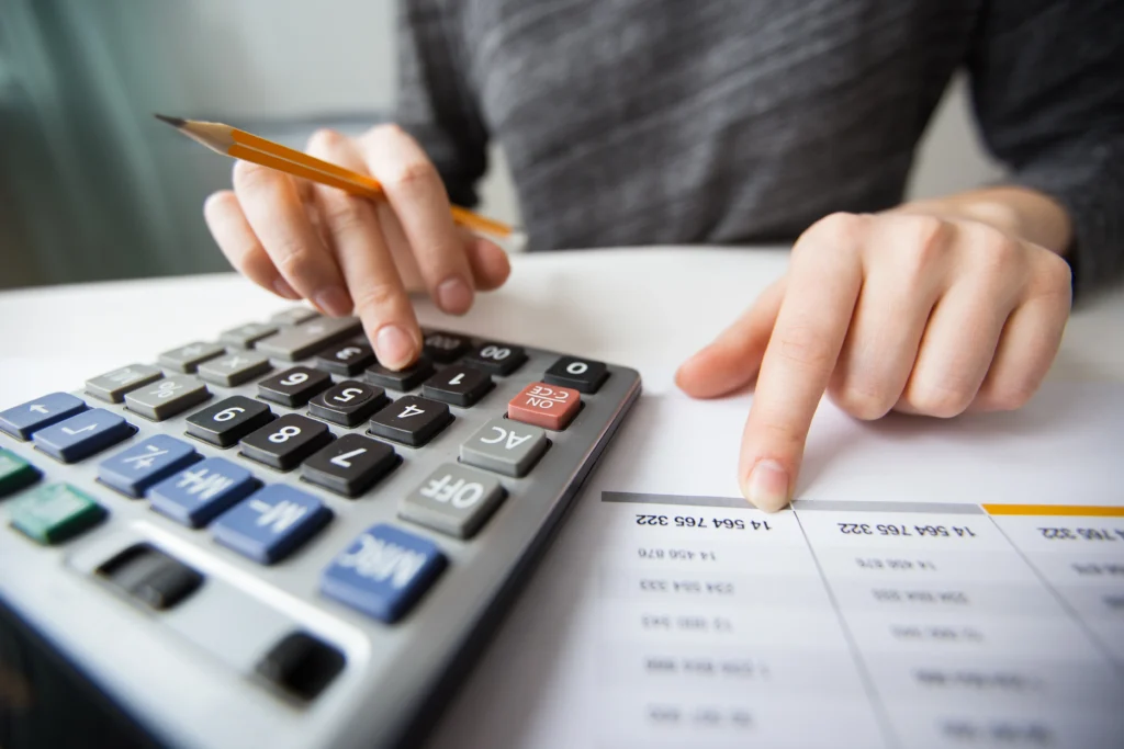 Pessoa usando calculadora e analisando uma planilha para definir o preço de venda de produtos