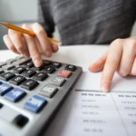 Pessoa usando calculadora e analisando uma planilha para definir o preço de venda de produtos