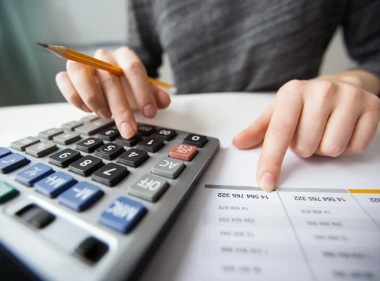 Pessoa usando calculadora e analisando uma planilha para definir o preço de venda de produtos