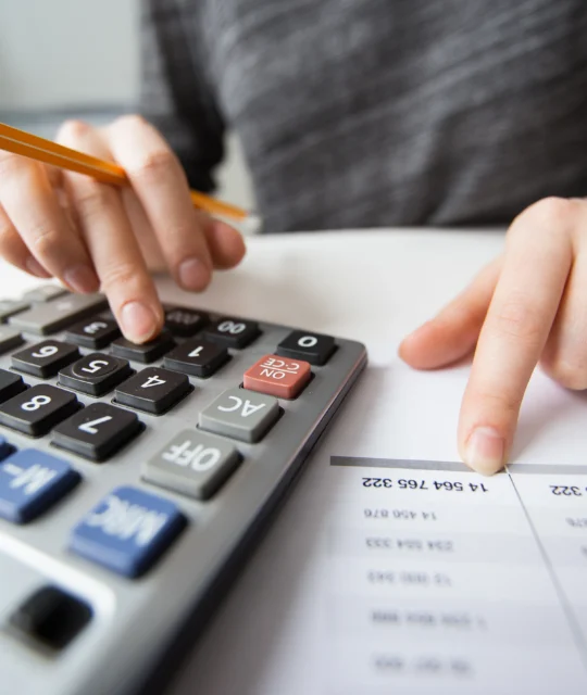 Pessoa usando calculadora e analisando uma planilha para definir o preço de venda de produtos
