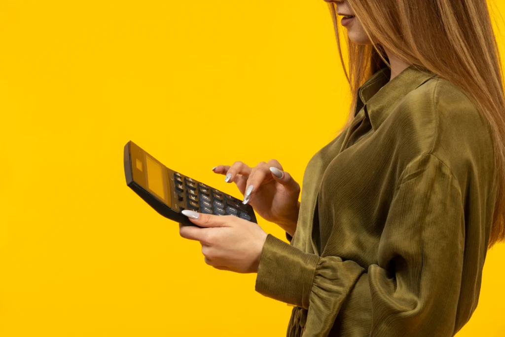 Mulher usando uma calculadora para fazer a precificação de produtos sobre fundo amarelo