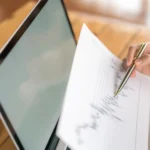 Pessoa analisando uma folha com dados e gráficos ao lado de um notebook, representando o uso do histórico de preços Black Friday para planejar promoções e definir descontos