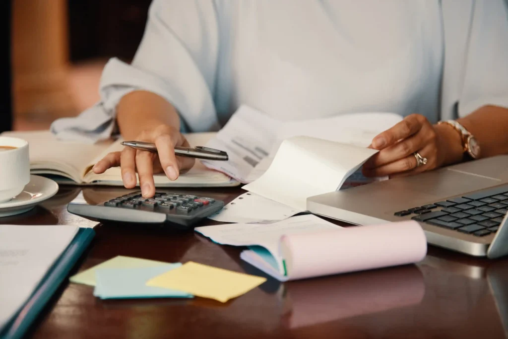 Pessoa usando calculadora ao lado de recibos, documentos e notebook