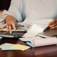 Pessoa usando calculadora ao lado de recibos, documentos e notebook