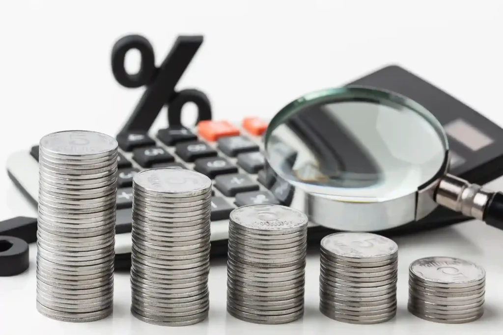 Pilhas de moedas ao lado de calculadora, lupa e símbolo de porcentagem