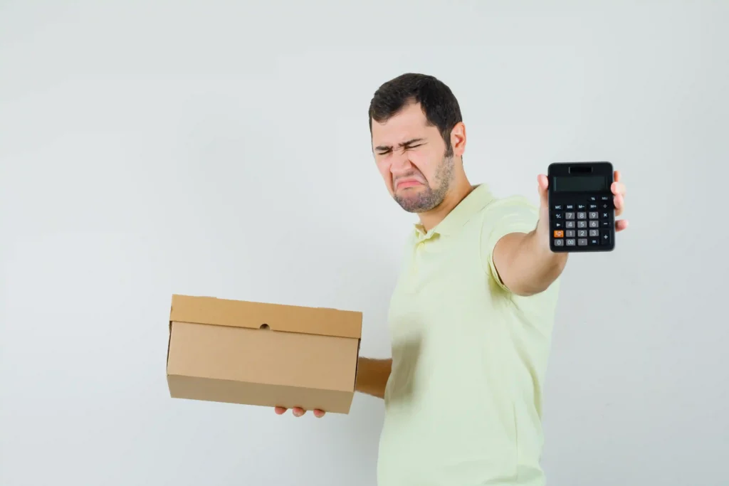 Homem segurando uma caixa de papelão e mostrando uma calculadora, com expressão de preocupação, representando os desafios do cálculo de estoque de segurança