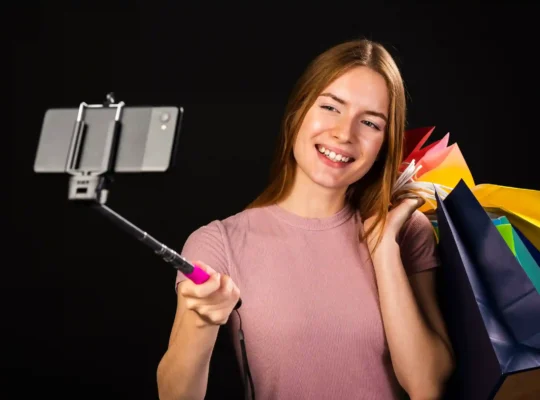 Mulher grava vídeo com celular enquanto segura sacolas de compras, representando a descoberta de produtos na Black Friday 2026