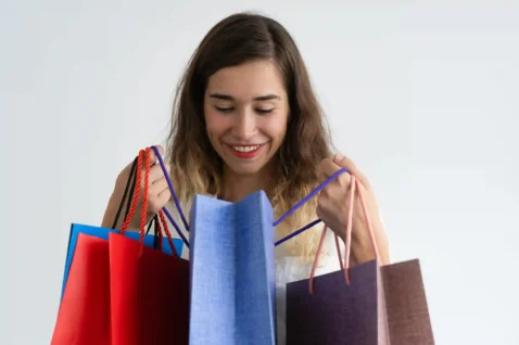 Mulher sorridente segurando sacolas de compras coloridas sobre fundo branco