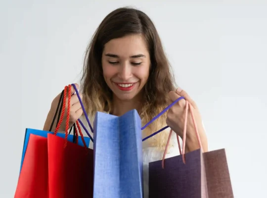 Mulher sorridente segurando sacolas de compras coloridas sobre fundo branco
