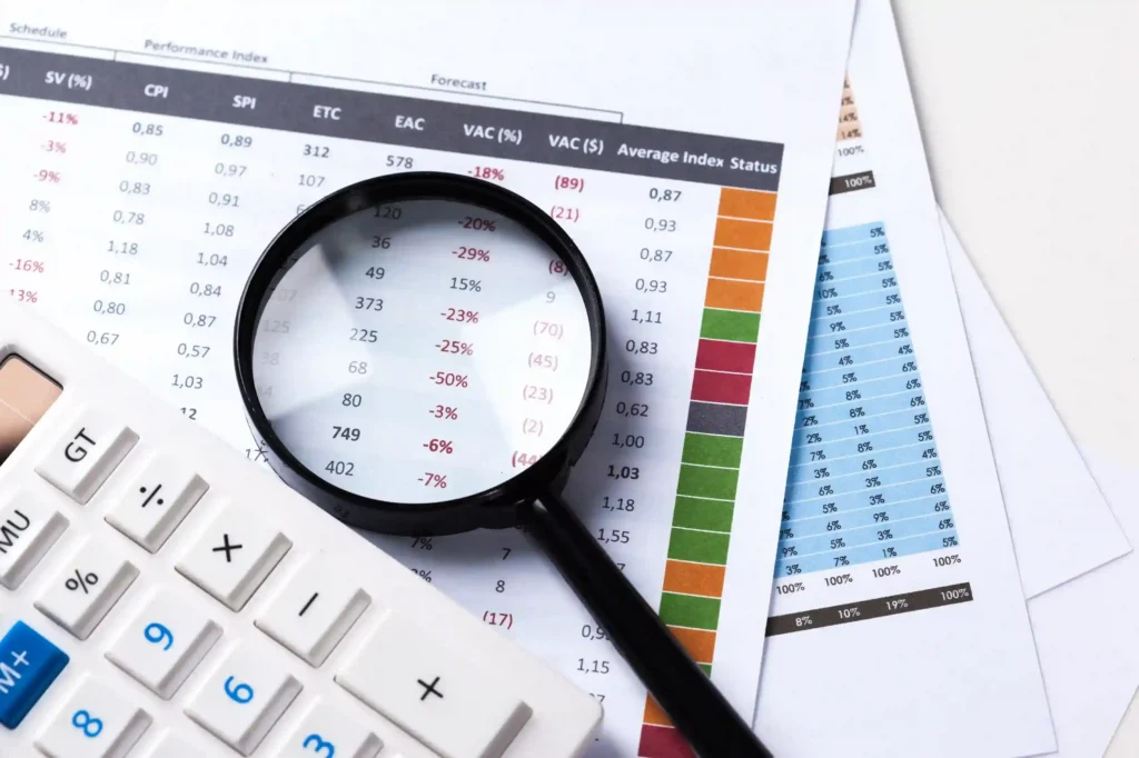 Lupa sobre planilhas com números, porcentagens e indicadores de desempenho, ao lado de uma calculadora