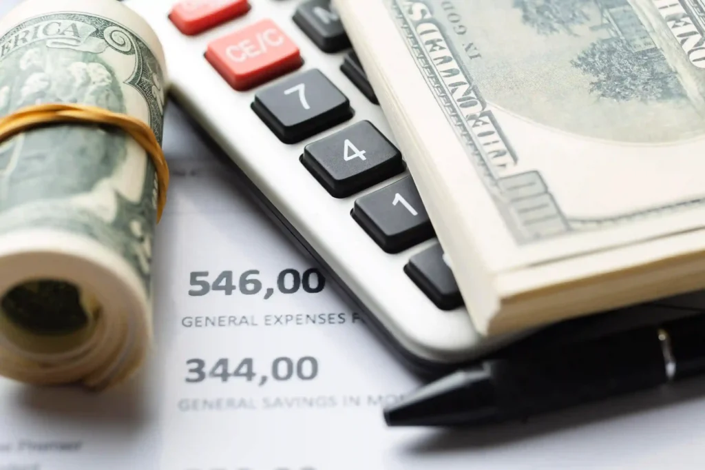 Notas de dólar sobre calculadora e planilha de despesas representando o impacto do câmbio nos custos de importação