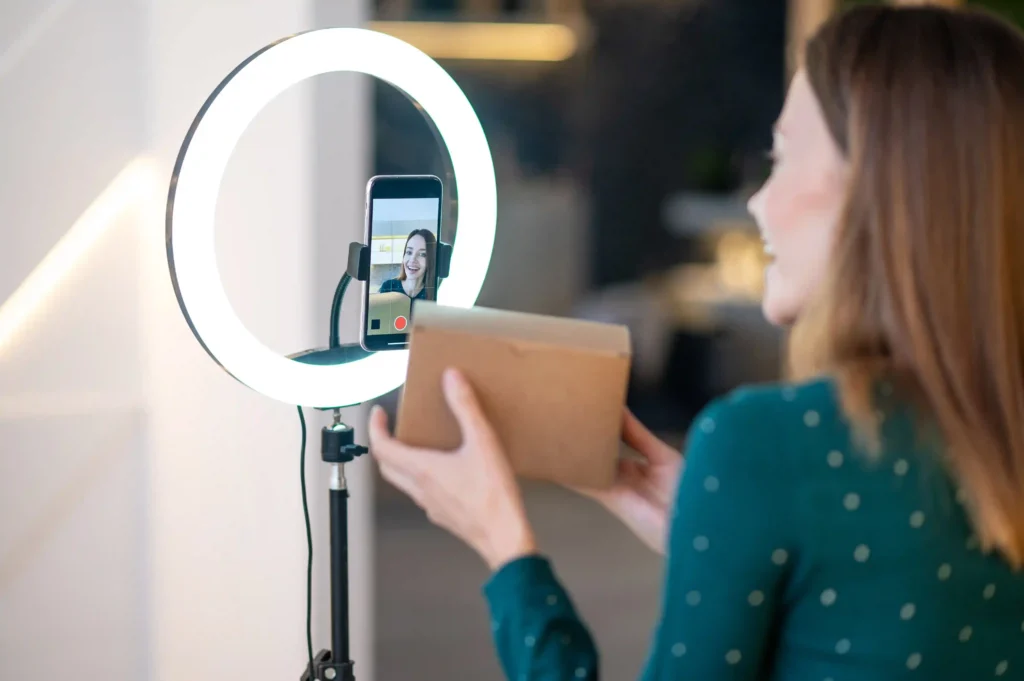 Mulher apresenta uma caixa diante do celular com ring light durante uma transmissão de live commerce