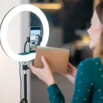 Mulher apresenta uma caixa diante do celular com ring light durante uma transmissão de live commerce