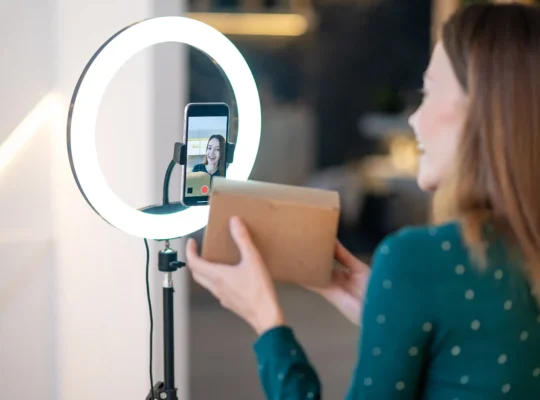 Mulher apresenta uma caixa diante do celular com ring light durante uma transmissão de live commerce