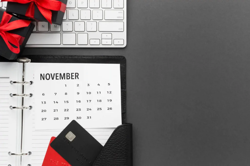 Calendário de novembro em uma agenda aberta, acompanhado de teclado, cartões de crédito e caixas de presente com laços vermelhos