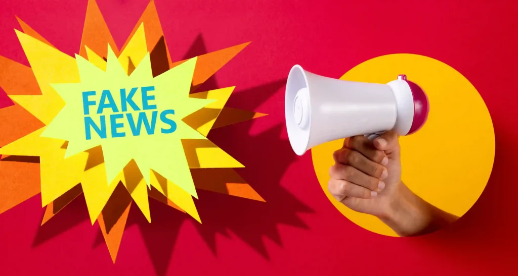 Mão segurando megafone branco ao lado da expressão Fake News sobre fundo vermelho