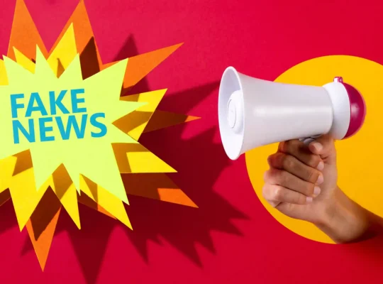 Mão segurando megafone branco ao lado da expressão Fake News sobre fundo vermelho